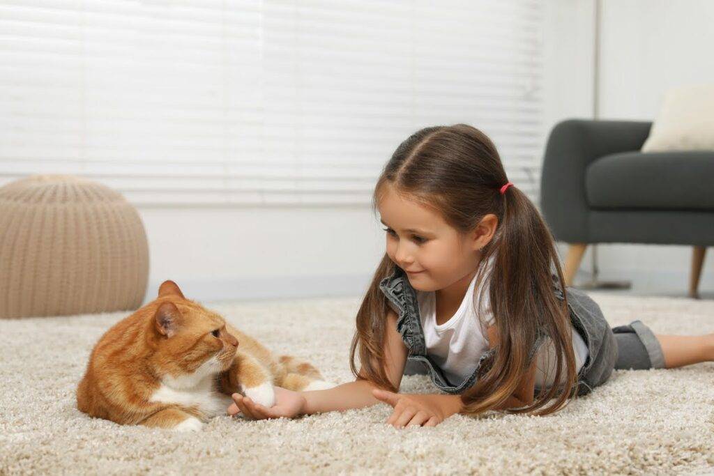 Happy child laying on a carpet and holding her cat's paw after the carpet was professionally cleaned by Amazing Results.