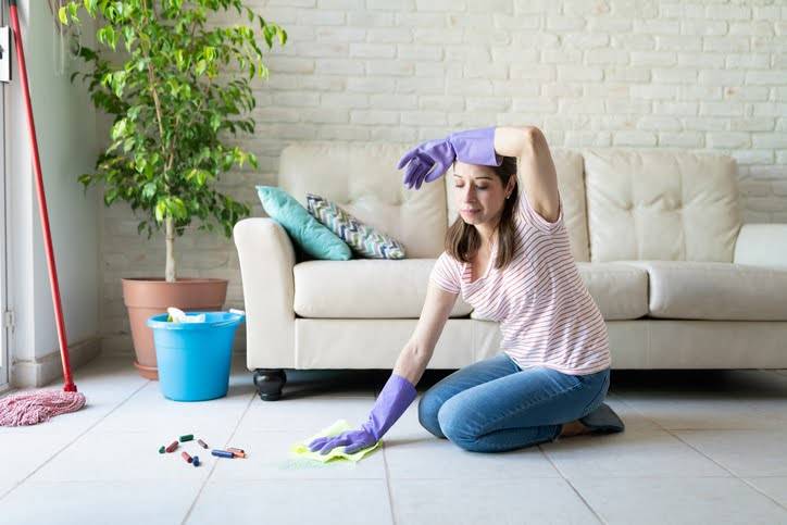 Woman on hands and knees trying to clean tile and grout with home cleaning solutions.